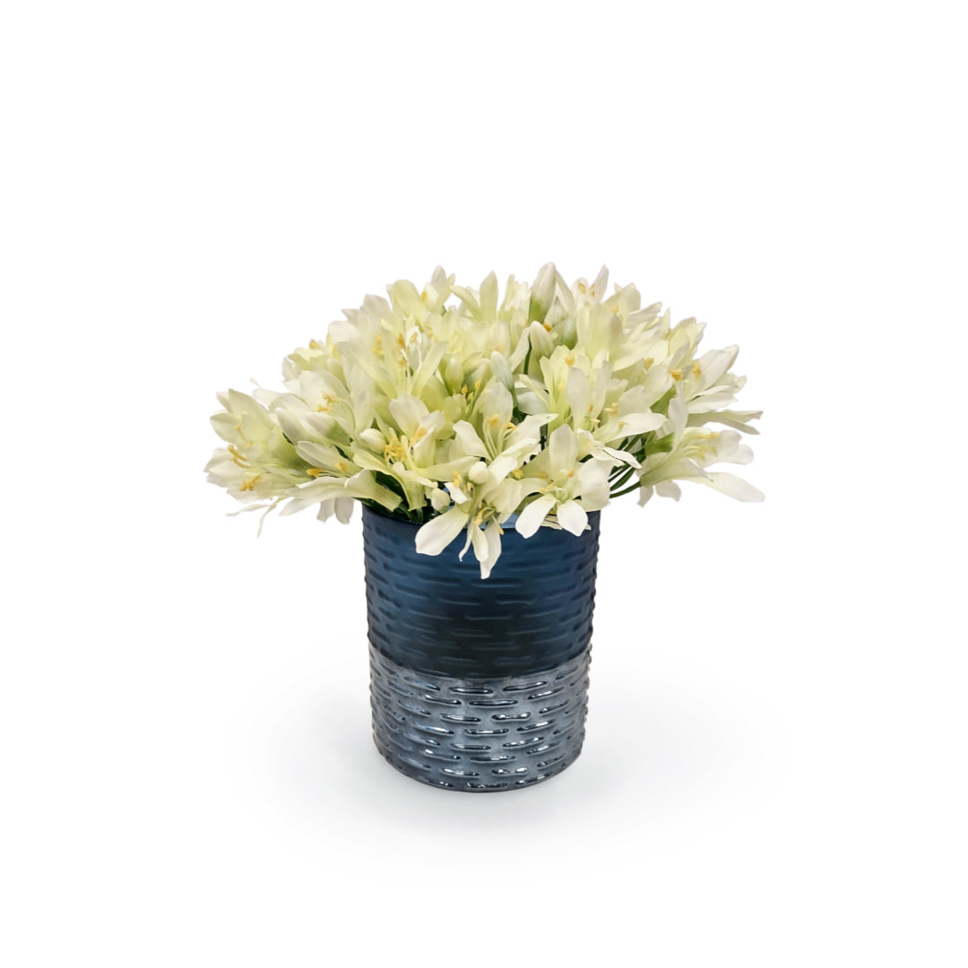Artificial white agapanthus flowers in textured blue glass vase on white background