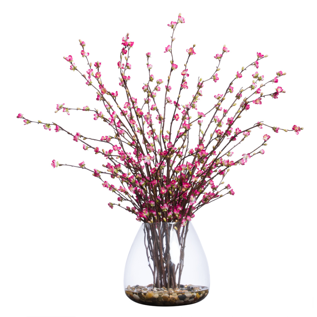Artificial cherry blossom branches with pink flowers in a clear glass vase with stones
