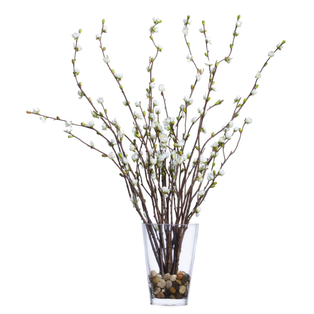 Artificial cherry blossom branches with white flowers in clear glass vase with pebbles