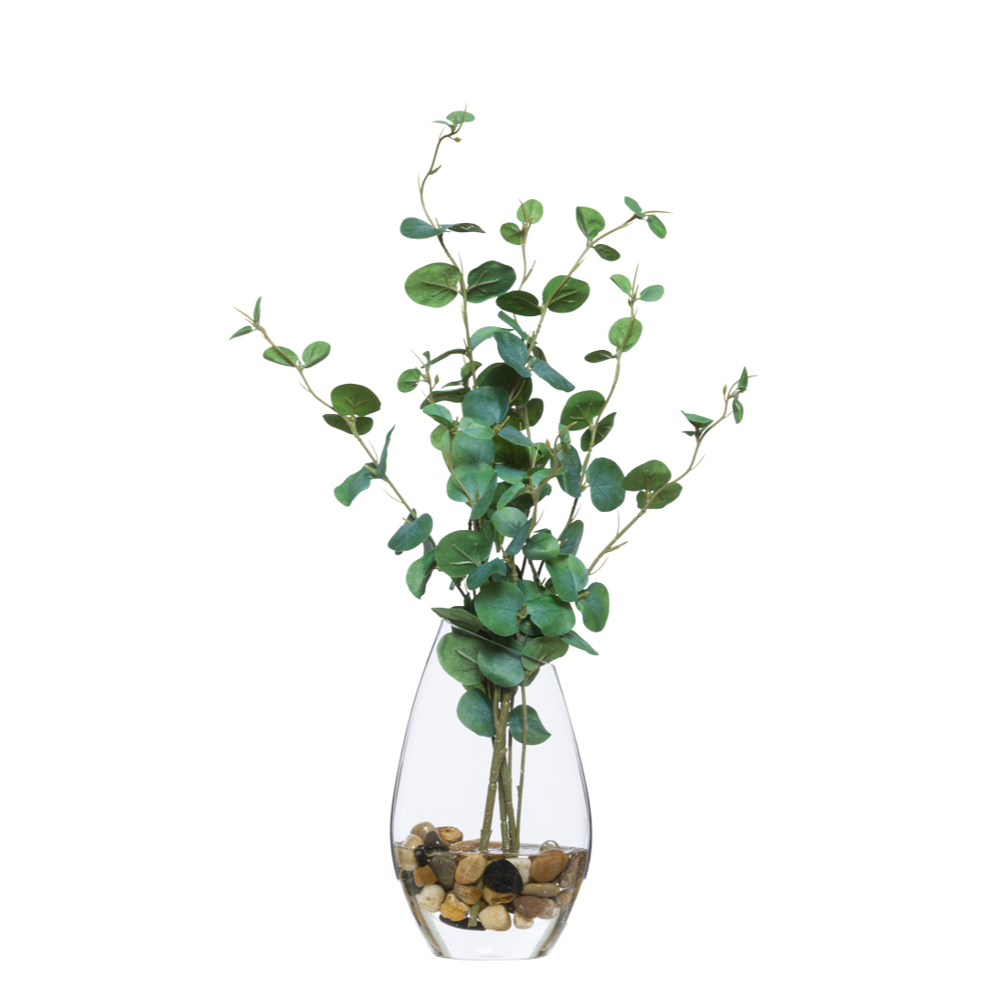 Artificial eucalyptus stems in a clear glass vase with decorative stones