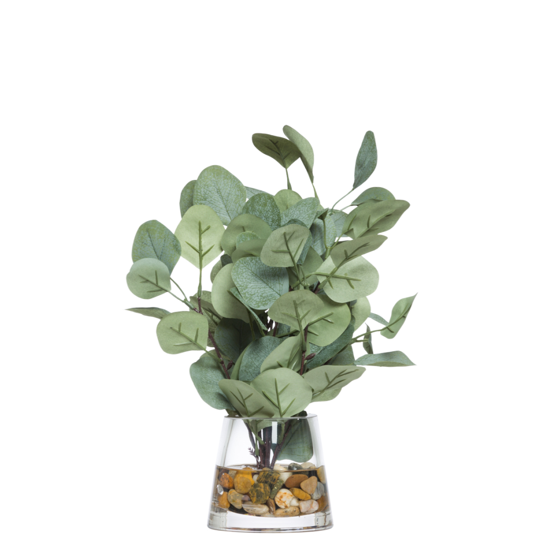 Artificial eucalyptus spray in glass vase with decorative stones, realistic faux greenery.