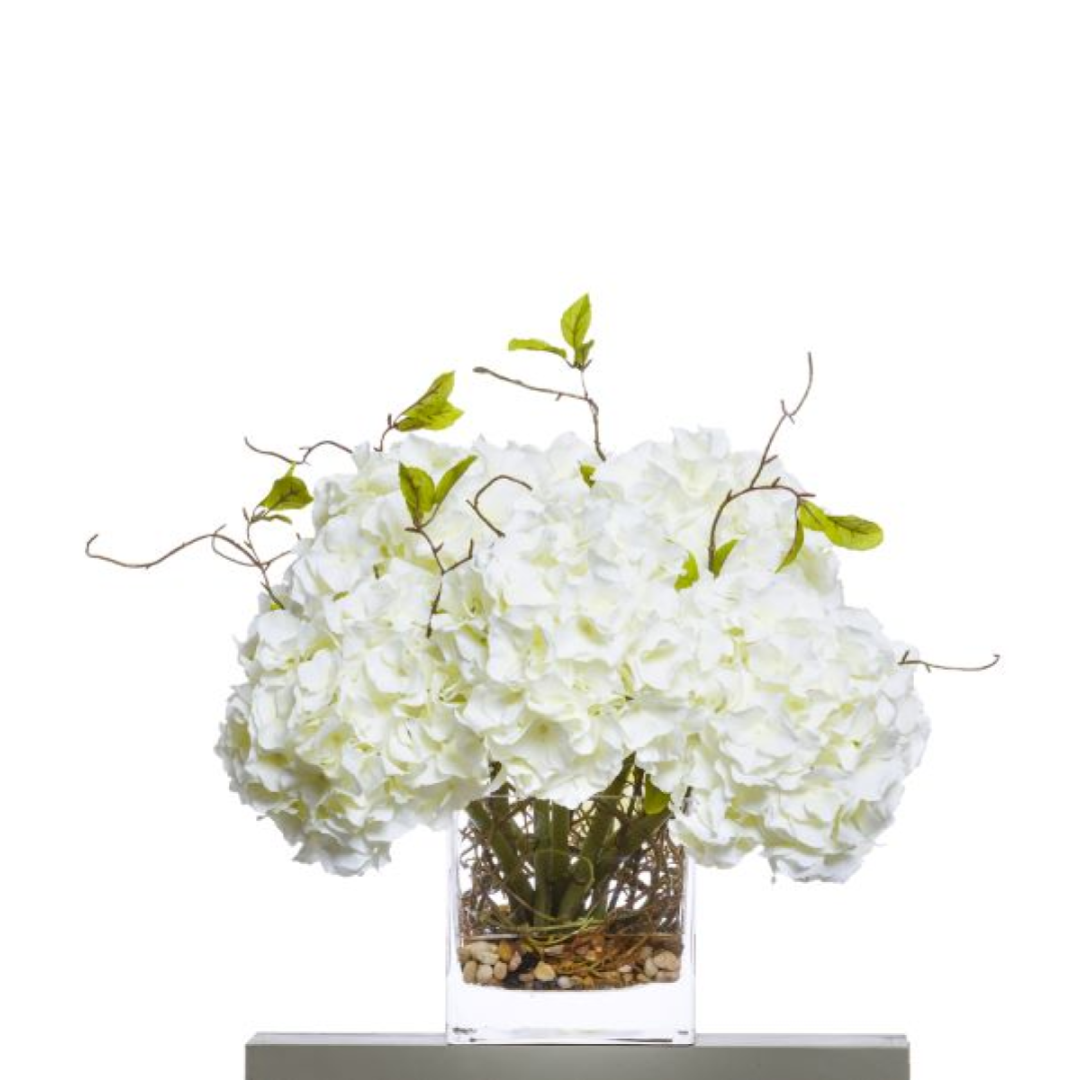 White hydrangea silk arrangement with willow branches in a glass vase with pebbles