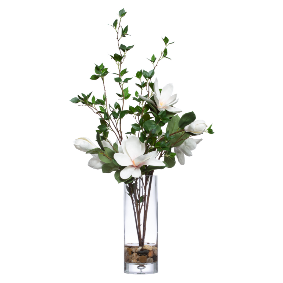 Artificial magnolia flower arrangement with white blooms in a clear glass vase with stones