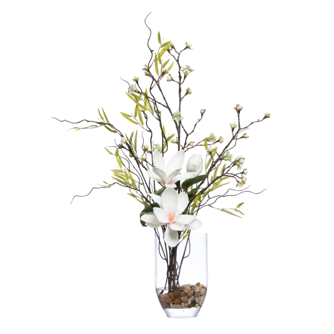 Artificial magnolia tree arrangement with white flowers in clear vase with pebbles