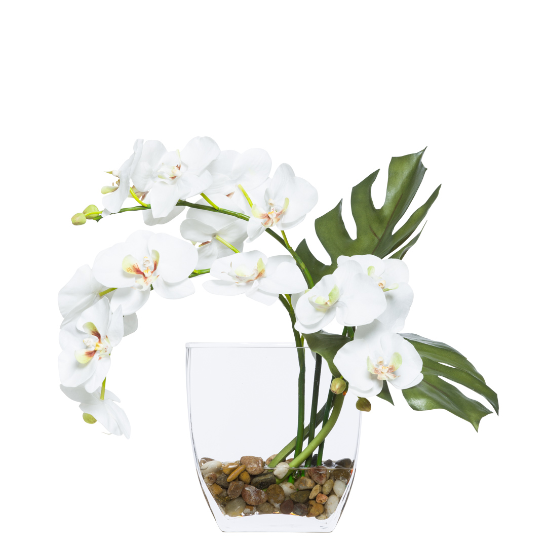 White artificial orchid arrangement in glass vase with green leaves and stones