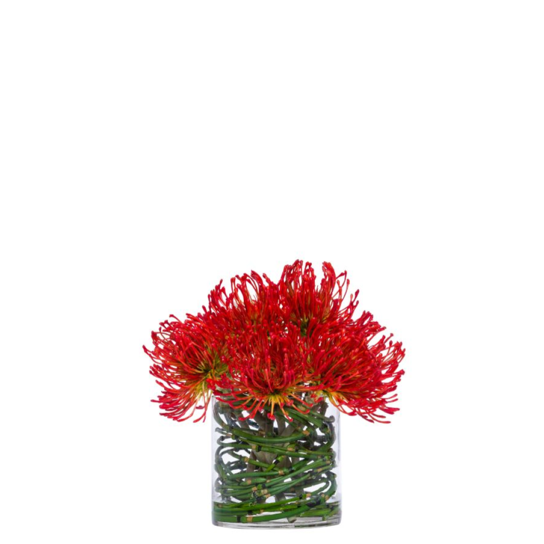 Red pincushion protea artificial flowers arranged in a clear glass vase