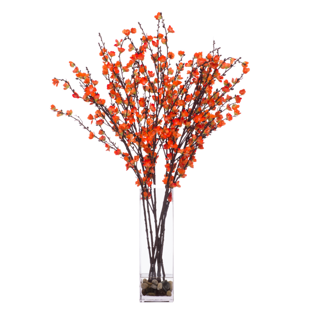 Artificial plum blossom branches with orange flowers in a tall glass vase with stones