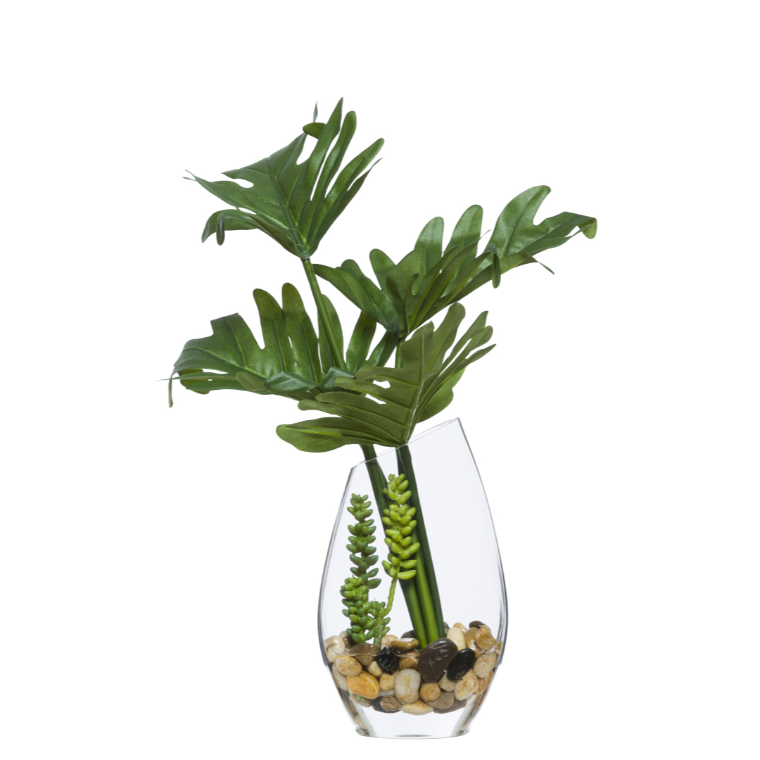Artificial selloum leaves and succulents in clear glass vase with decorative stones