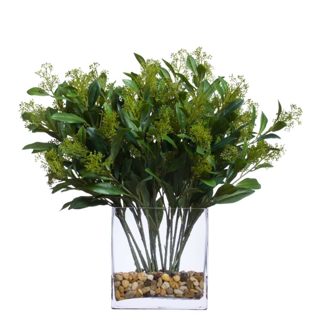 Artificial skimmia spray arrangement in clear glass vase with river rocks, realistic greenery