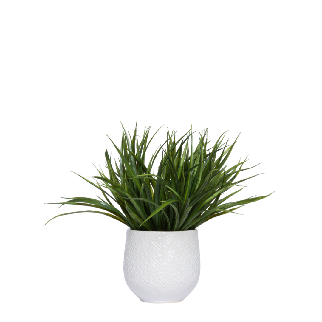 Artificial green grass plant in decorative white textured ceramic pot