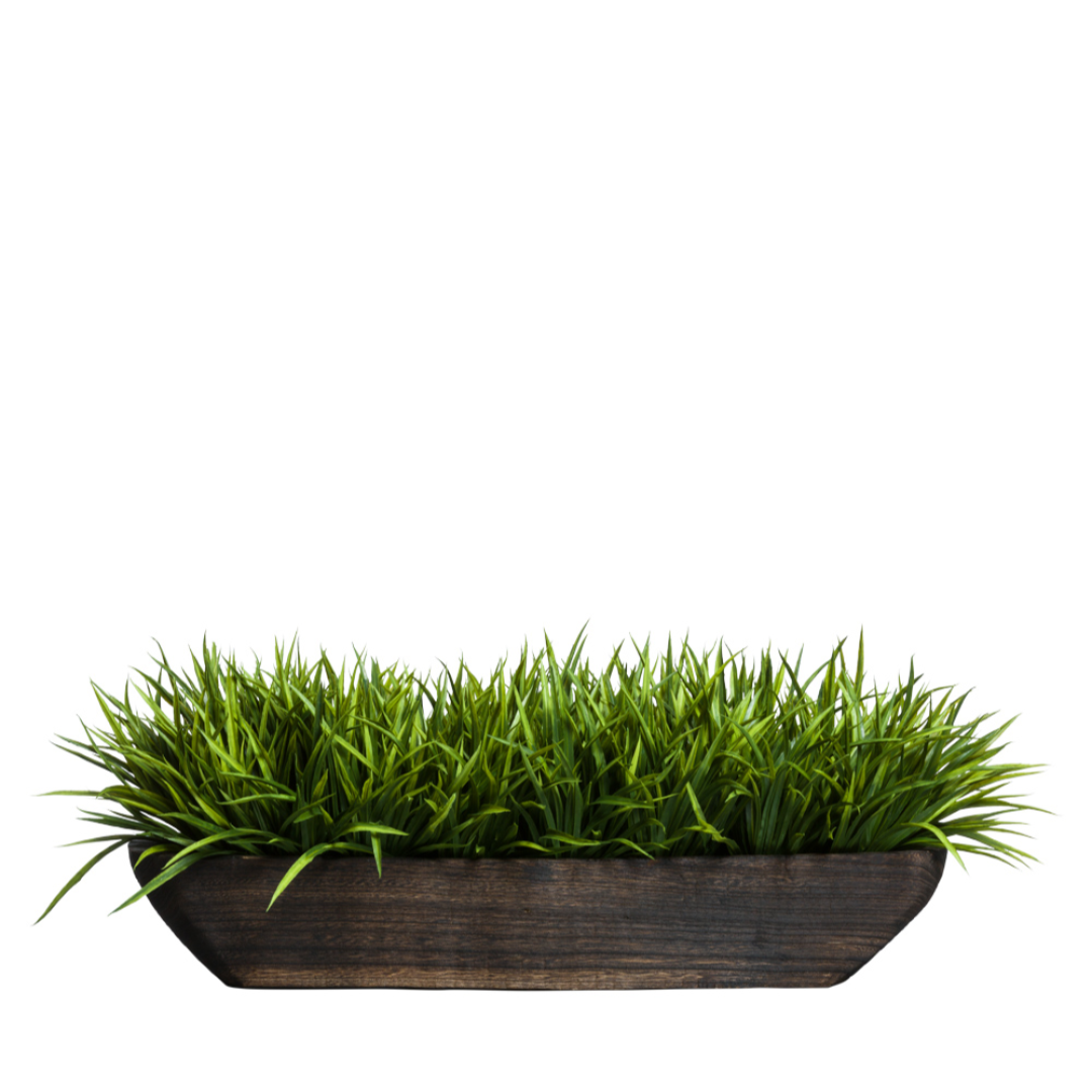 Artificial grass arrangement in long dark wooden planter on white background