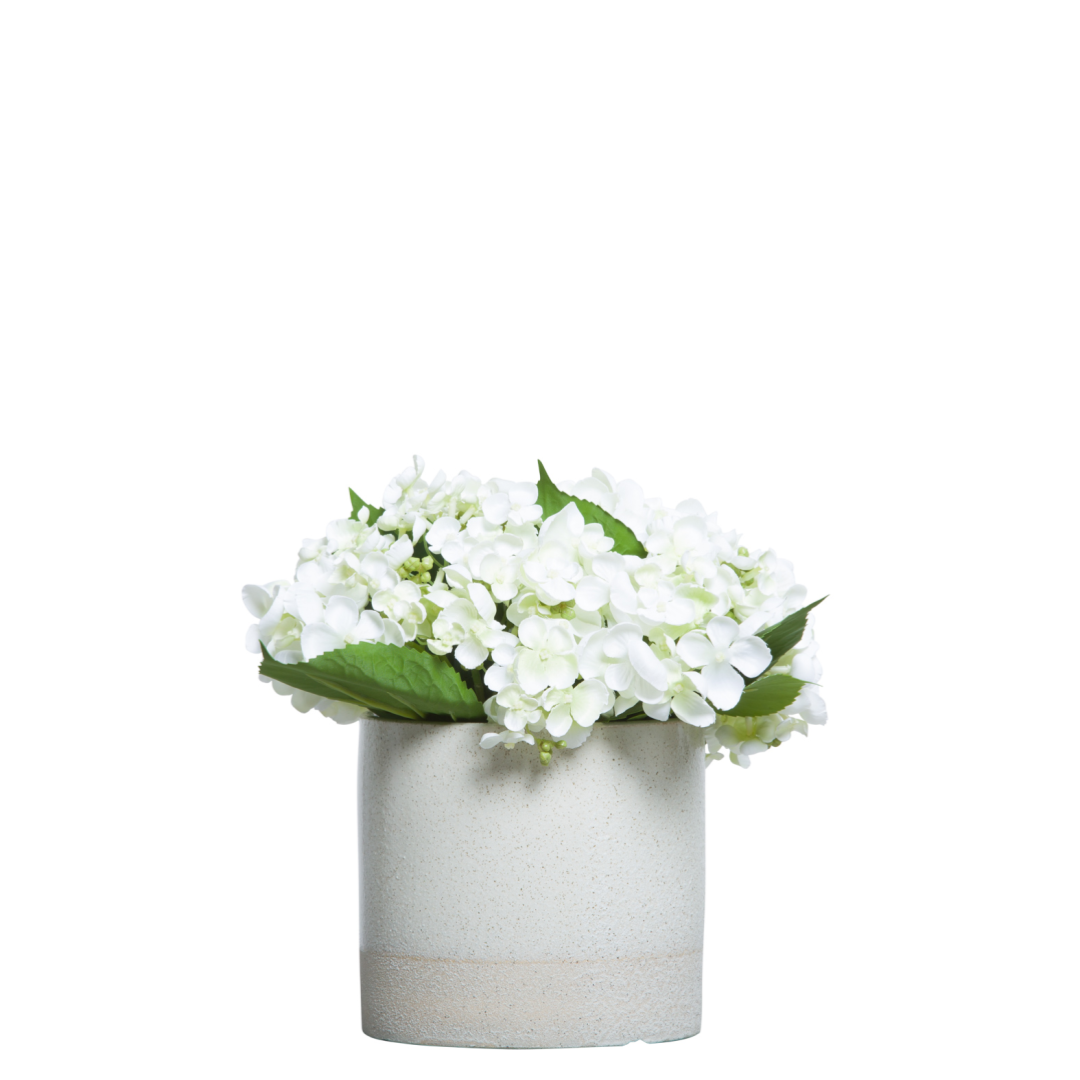 White hydrangea artificial flower arrangement in a modern ceramic pot with green leaves