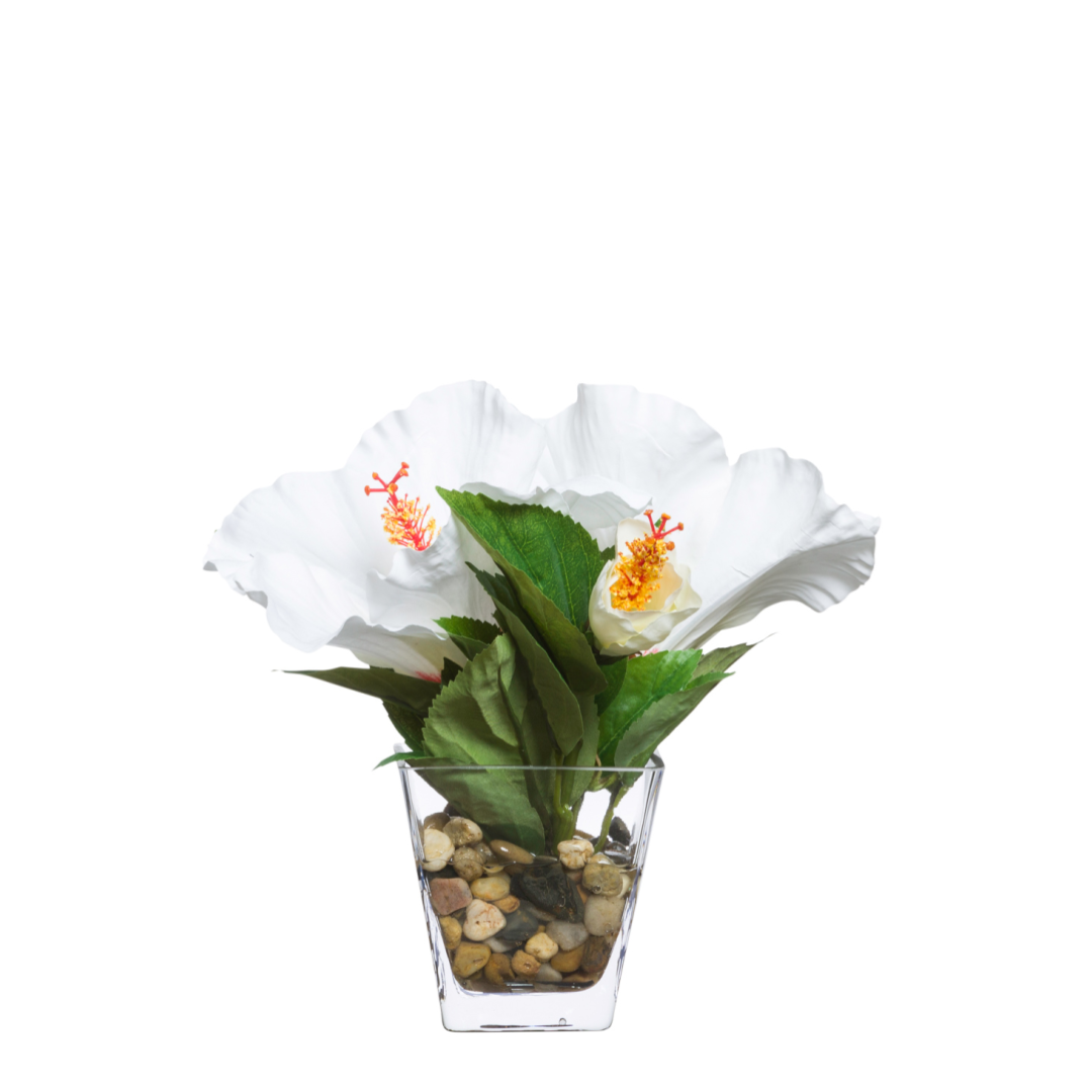 Artificial white hibiscus flowers with green leaves in a clear glass vase with pebbles