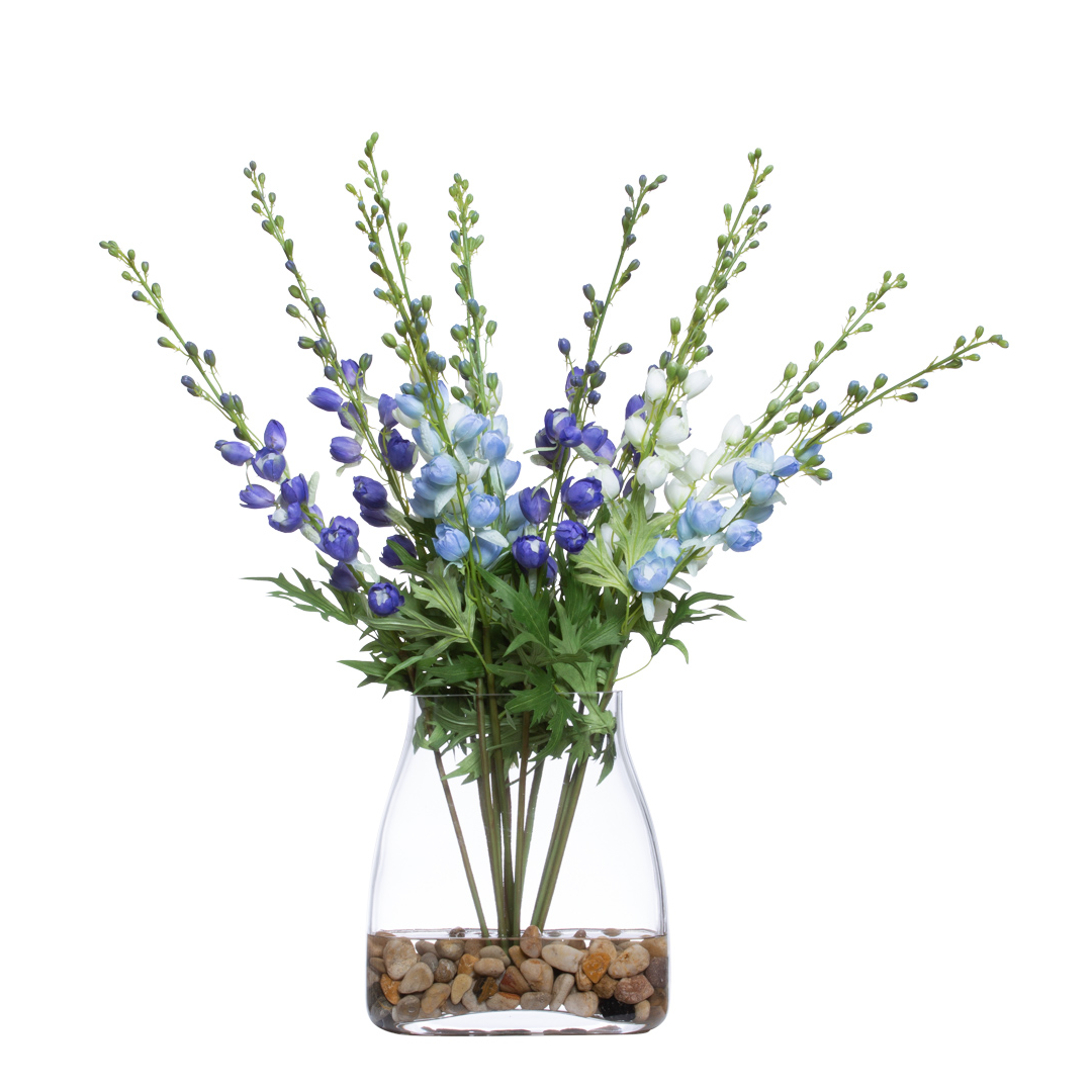 Artificial blue and white delphinium flowers in a clear vase with river pebbles