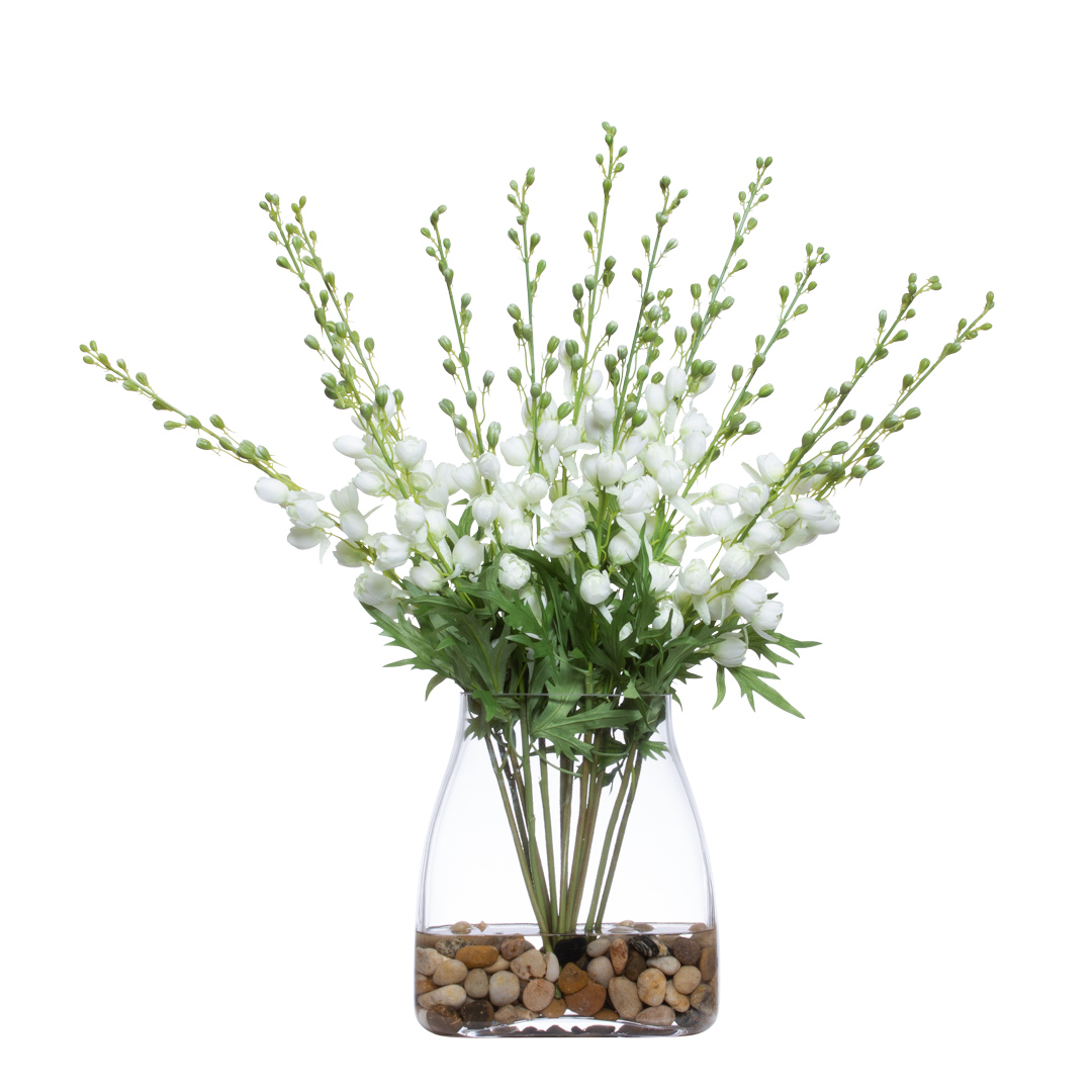 Artificial white floral arrangement with green leaves in a clear vase with pebbles