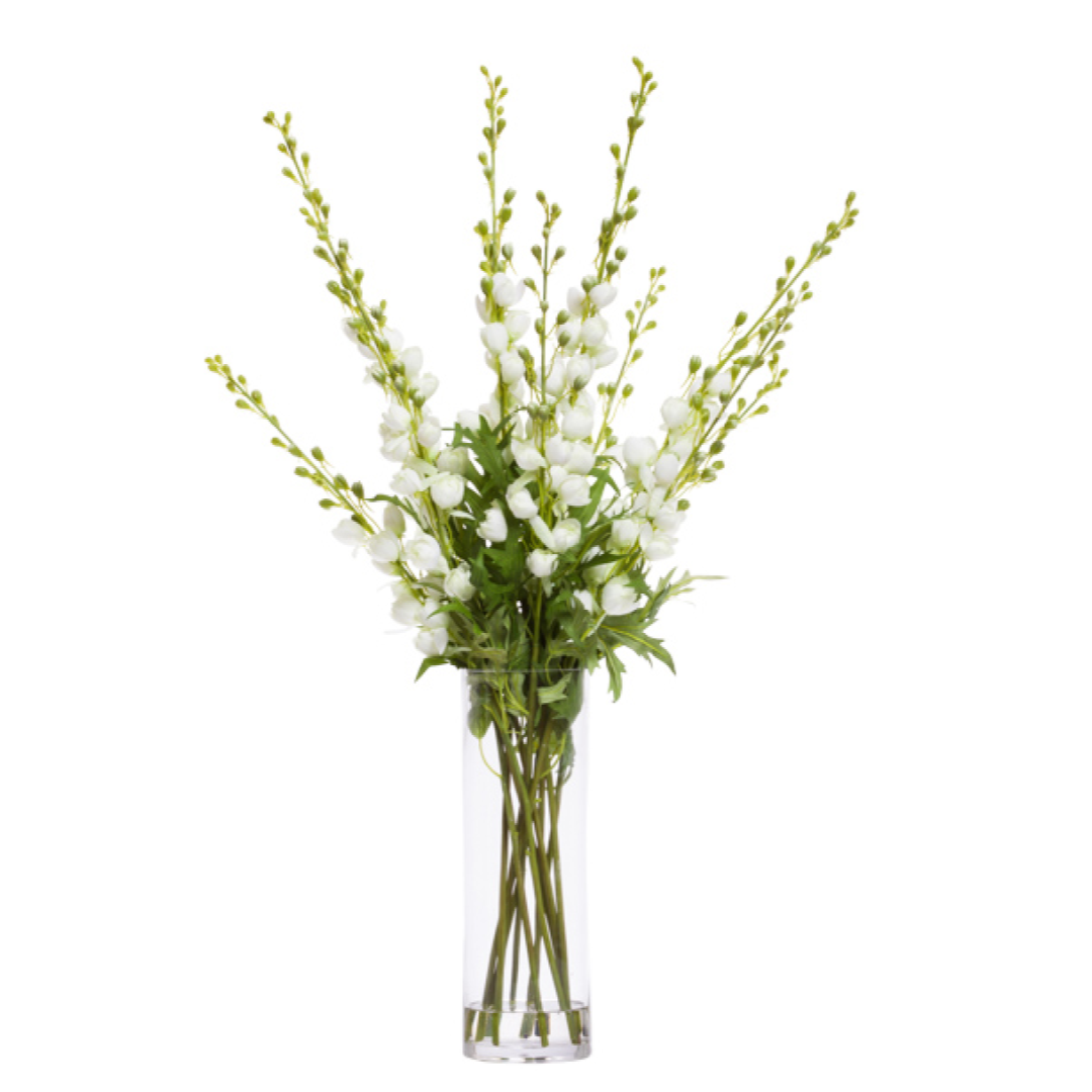 Artificial white floral arrangement in tall clear glass vase with green foliage