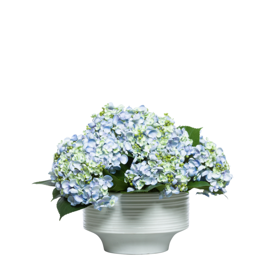 Artificial blue hydrangea arrangement in a white ceramic vase