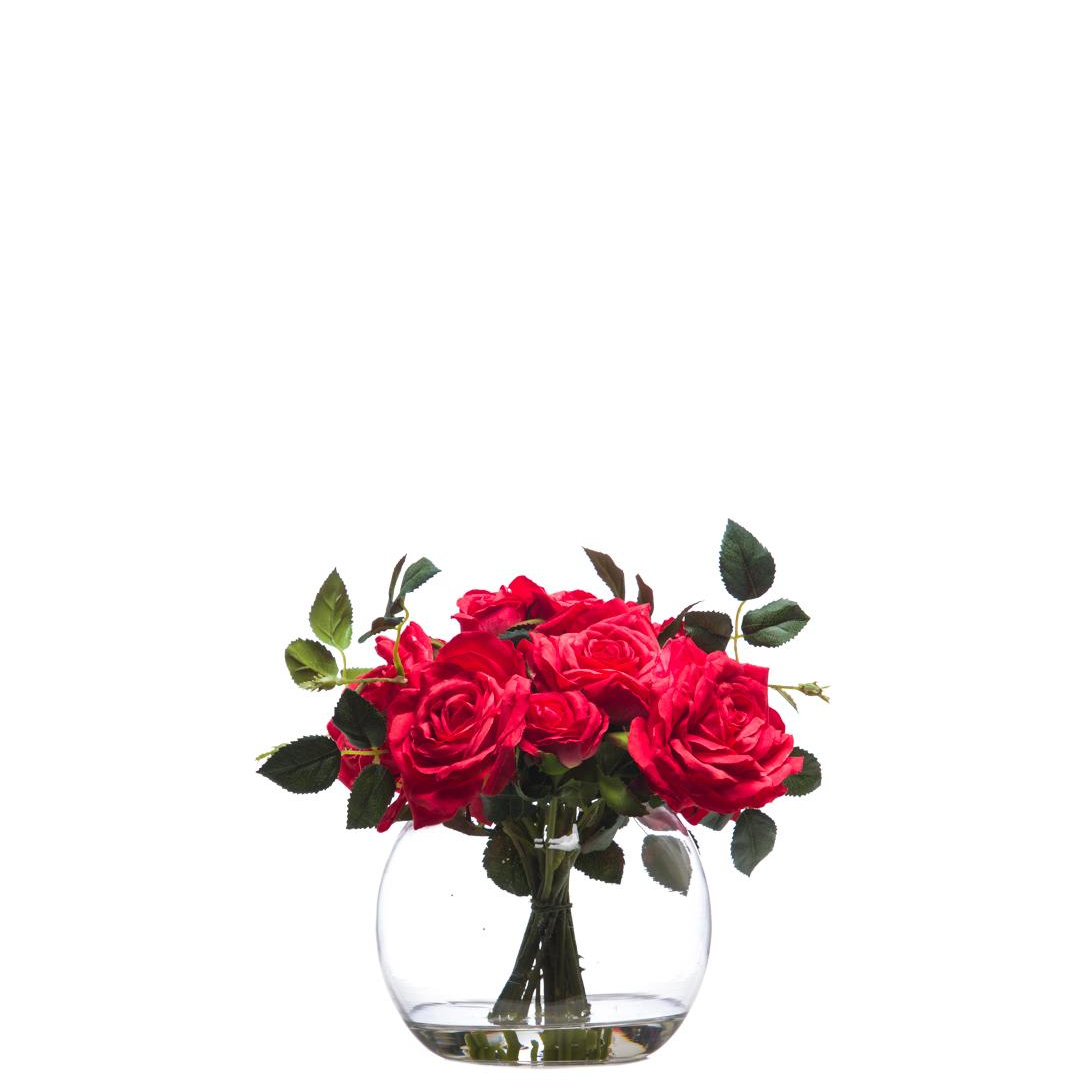 Artificial red rose bouquet in clear glass vase with green leaves, white background