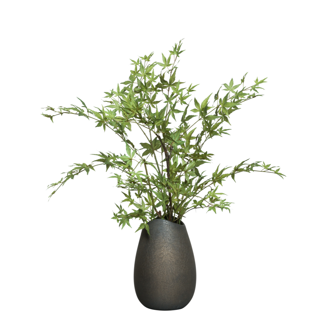 Artificial maple branches with green leaves in a textured black vase, isolated on white