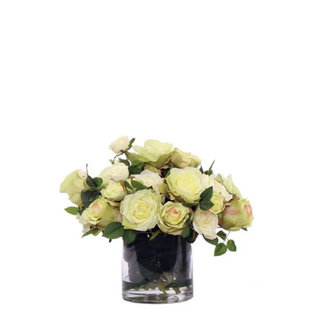 Artificial cream rose arrangement in a clear glass vase with green foliage