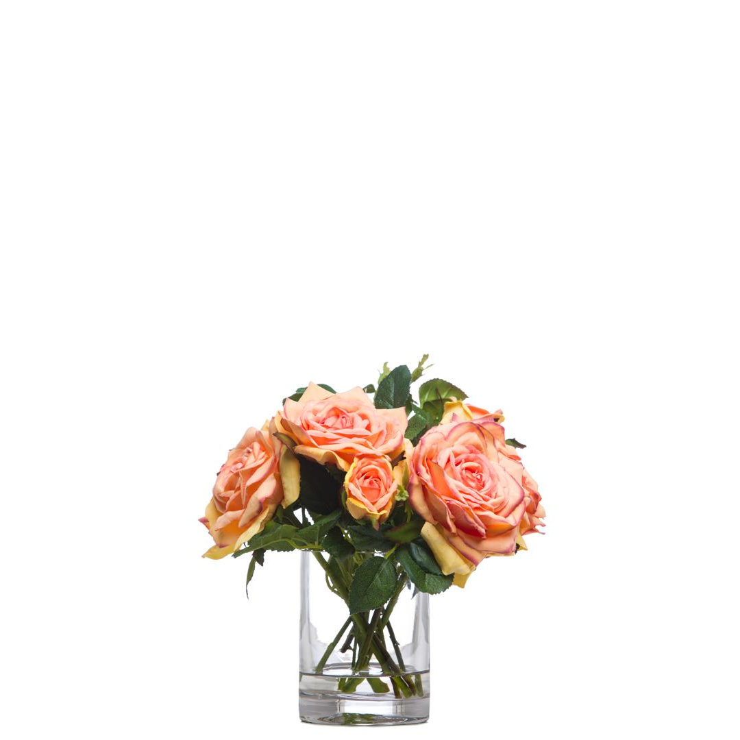 Realistic peach pink artificial roses in clear glass vase with green foliage