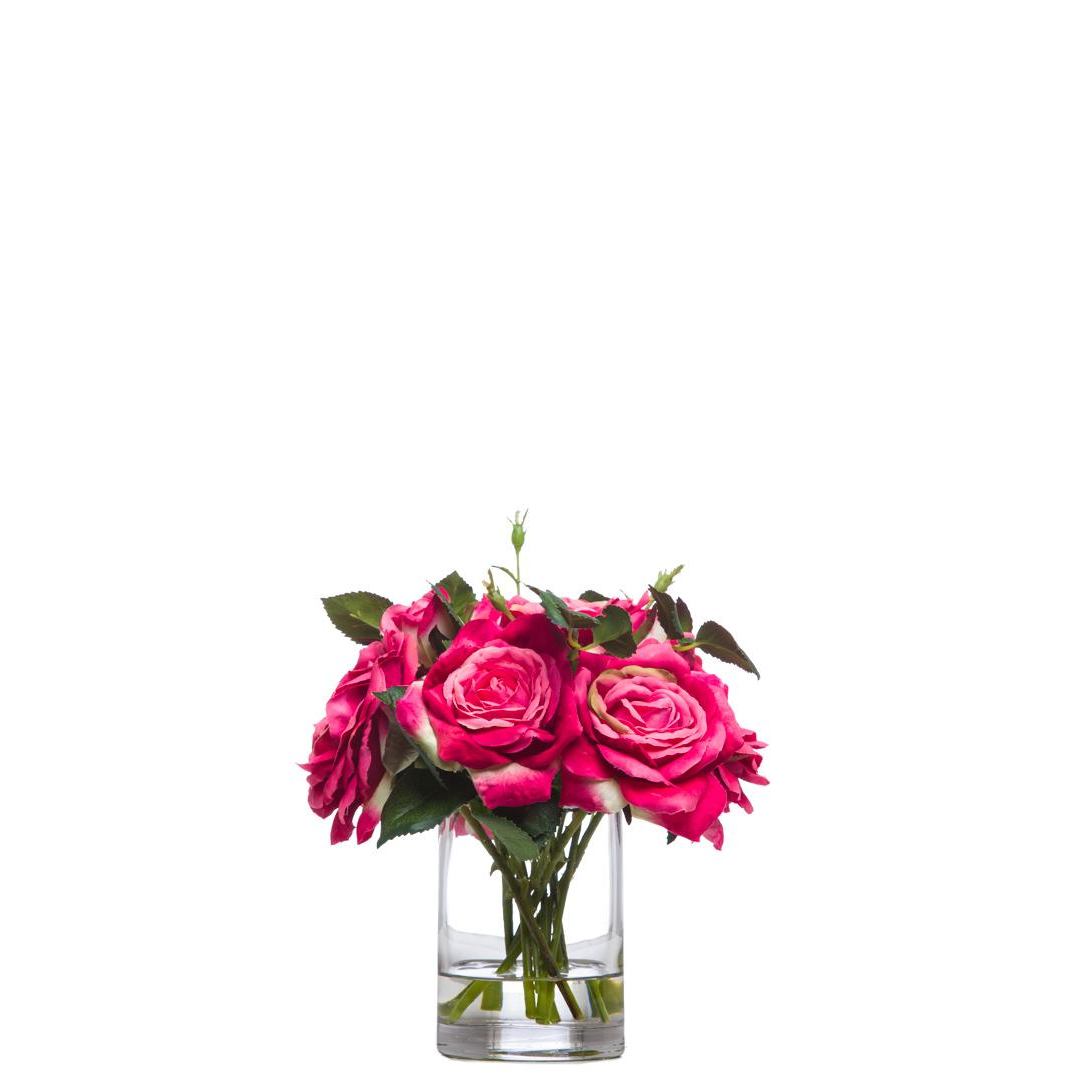 Pink artificial rose bouquet in a clear glass vase with green leaves, isolated on white