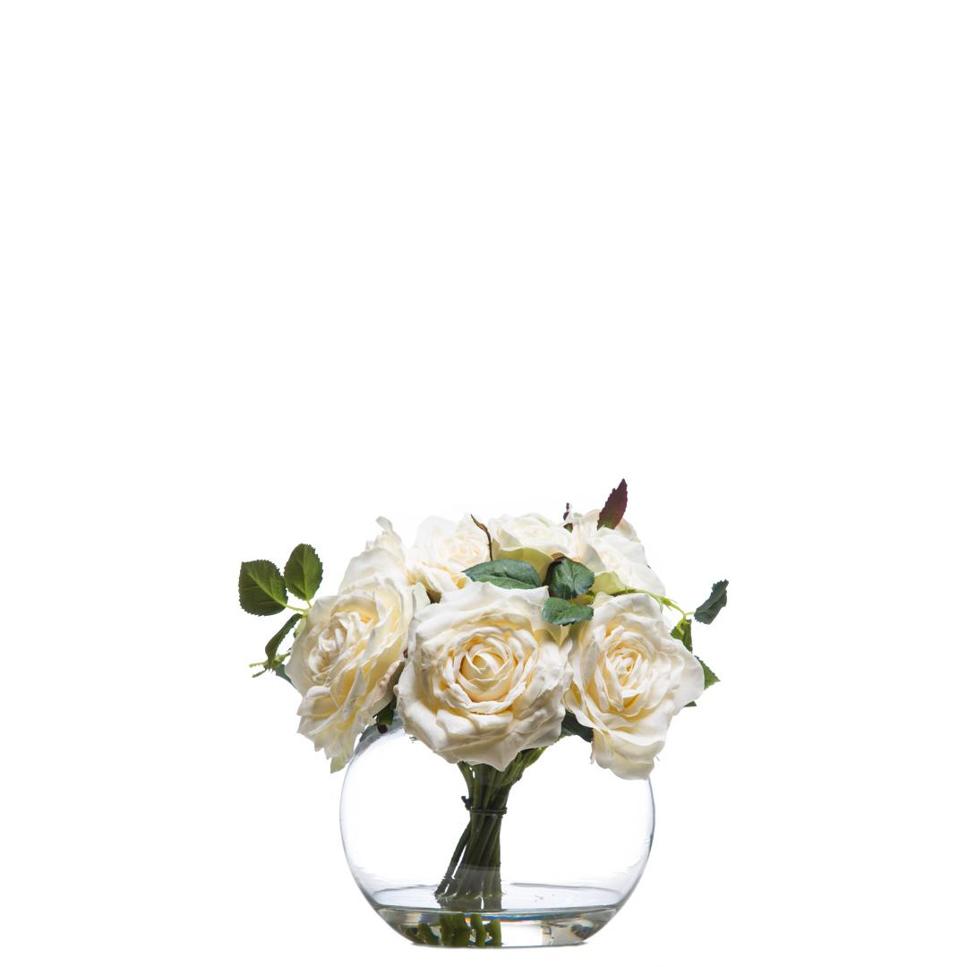 Artificial white rose bouquet in clear round glass vase with green leaves