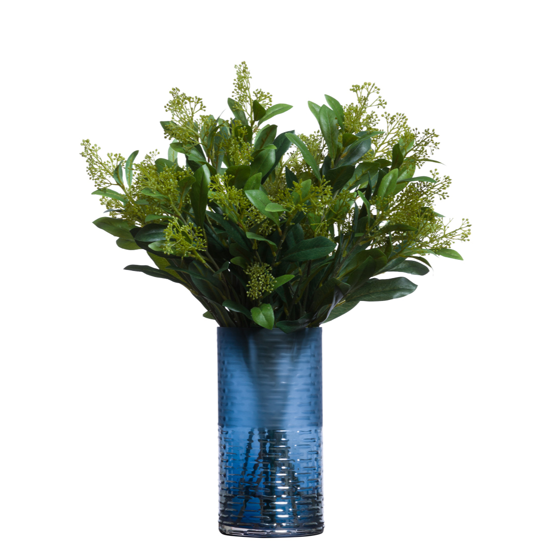 Artificial skimmia spray with green foliage in a textured blue glass vase