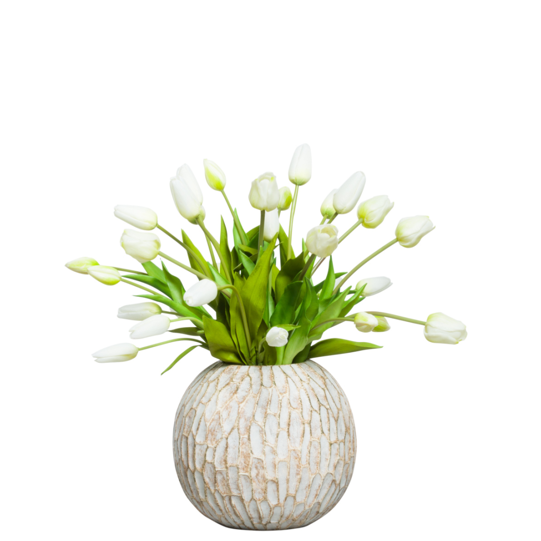 White tulip artificial flower arrangement in a round textured vase with green leaves