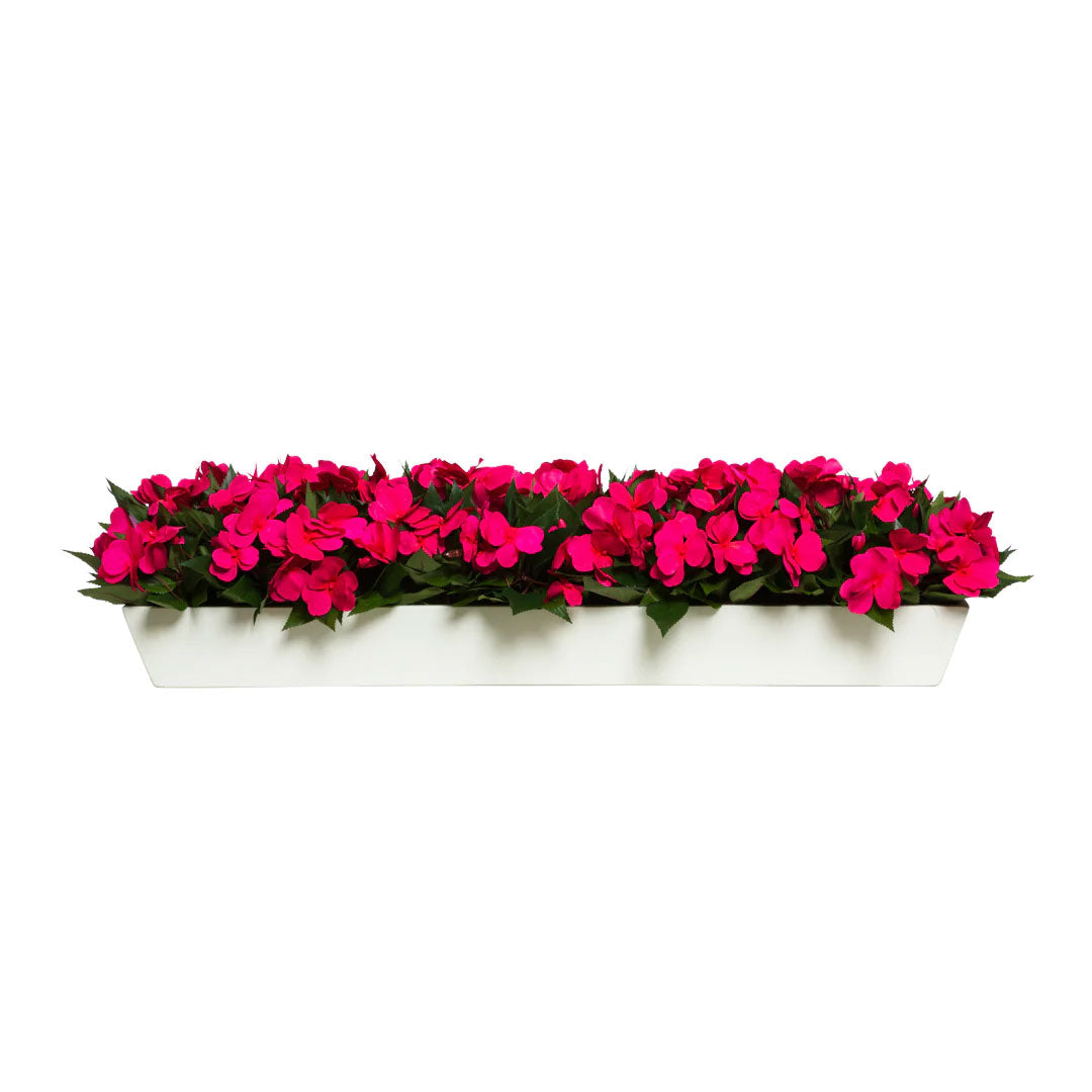Bright pink artificial flowers with green leaves in a rectangular white planter