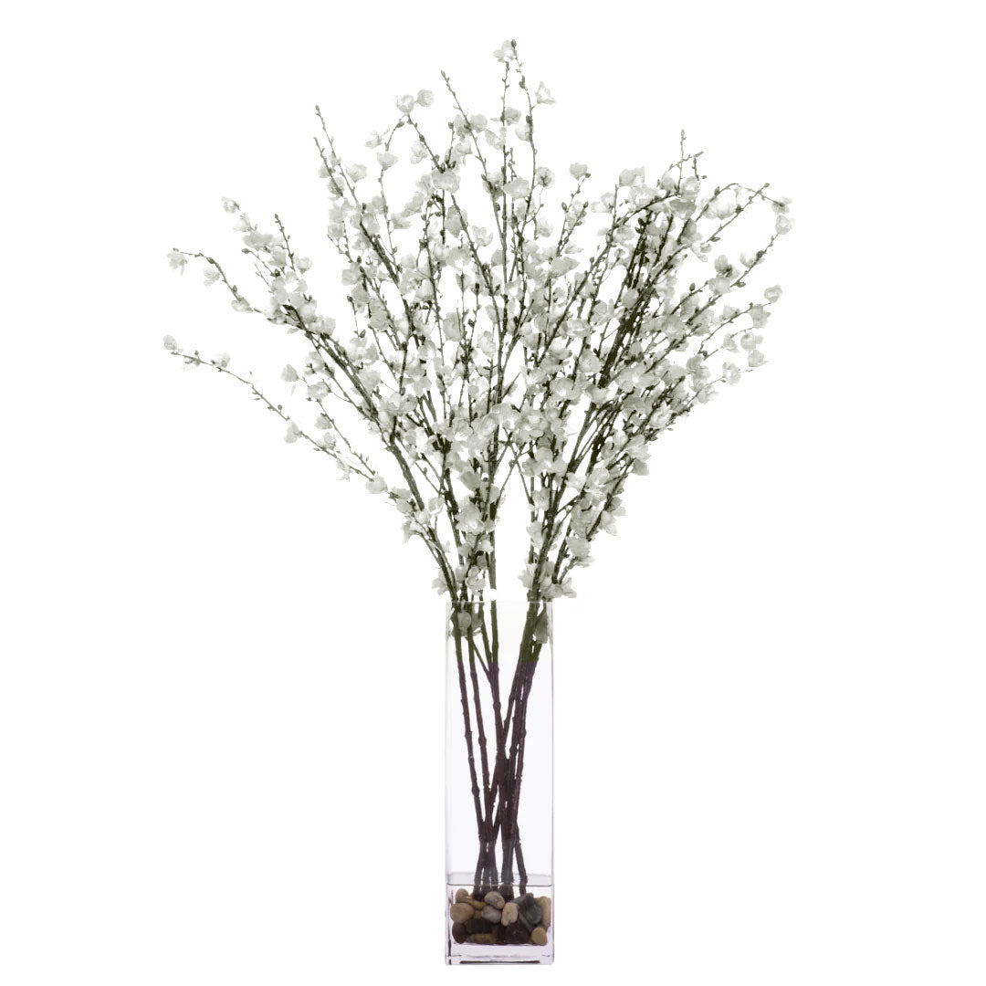Artificial white blossom branches in a clear glass vase with pebbles, modern floral decor