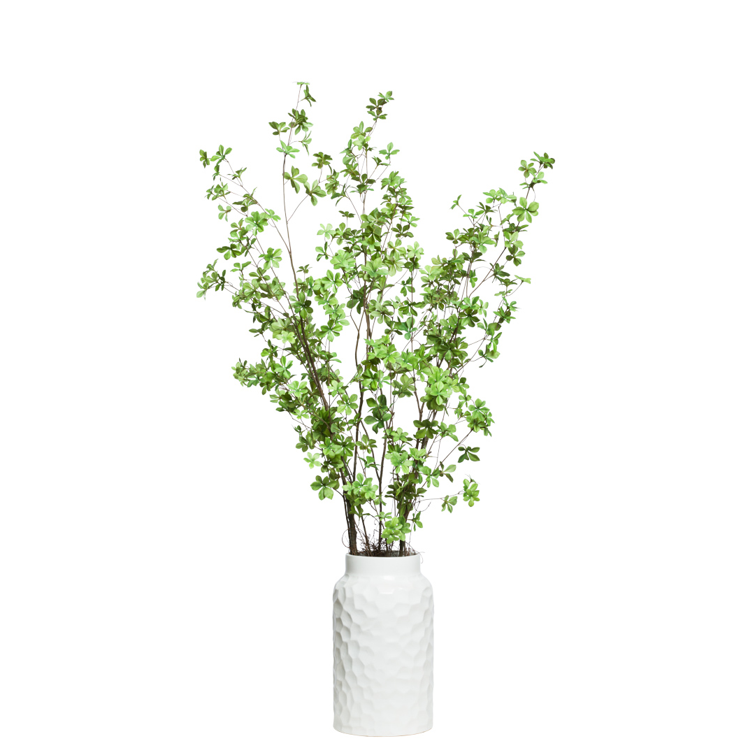 Artificial green leafy branches in textured white ceramic vase, botanical decor
