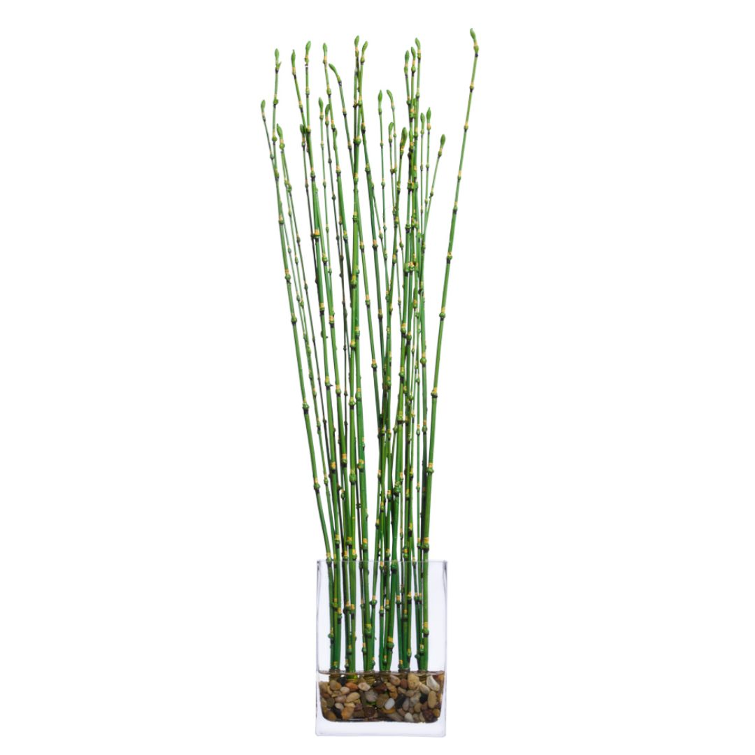Artificial bamboo stalks in a clear glass vase with pebbles, minimalist decor