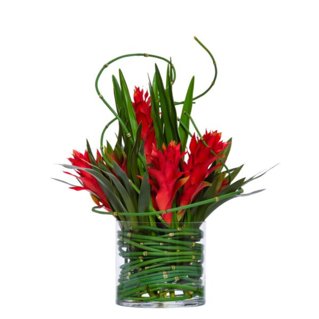 Artificial red bromeliad arrangement with green leaves in clear glass vase