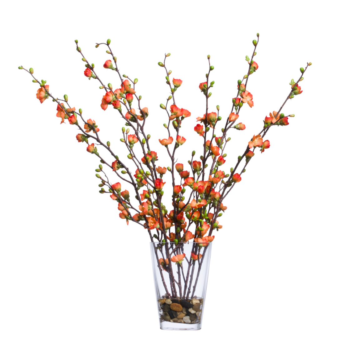 Artificial cherry blossom branches with orange flowers in clear glass vase with stones