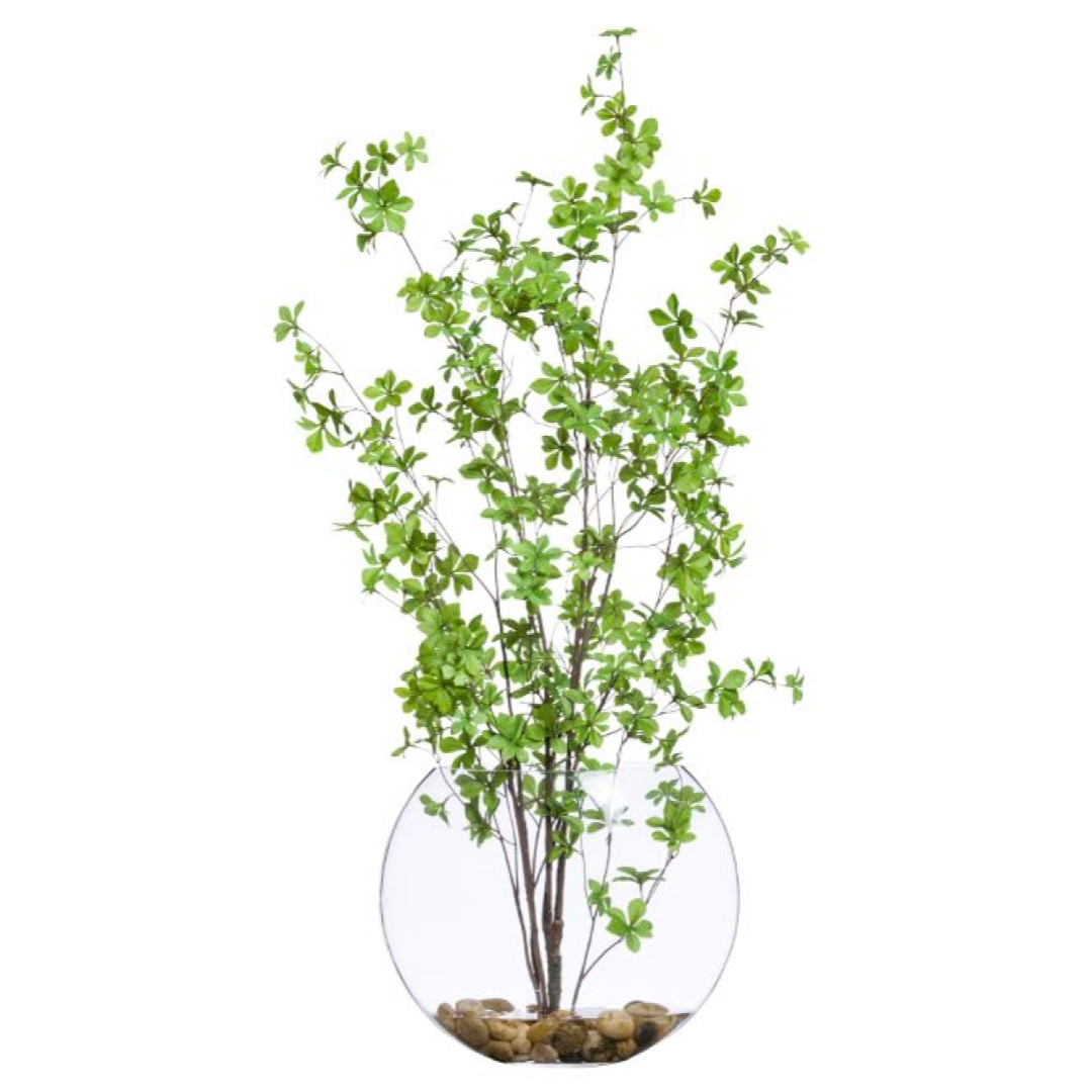 Artificial green leafy branches in a round clear glass vase with decorative rocks