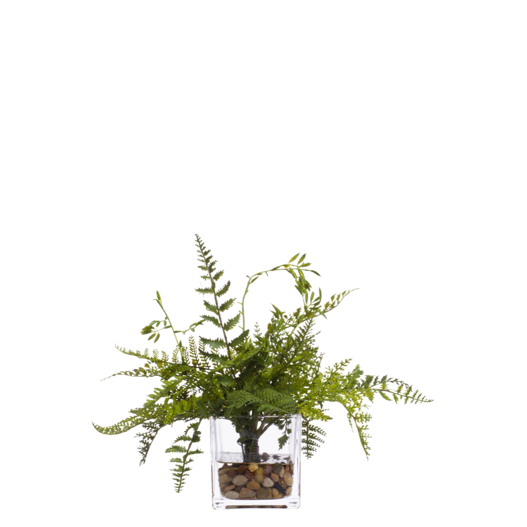 Artificial fern plant arrangement in a clear glass vase with pebbles on white background