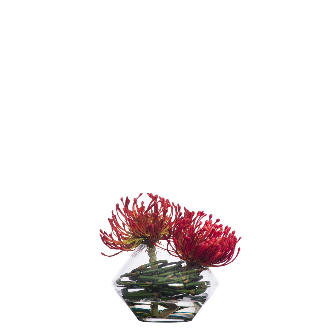 Artificial red pincushion protea flowers in a clear geometric glass vase arrangement