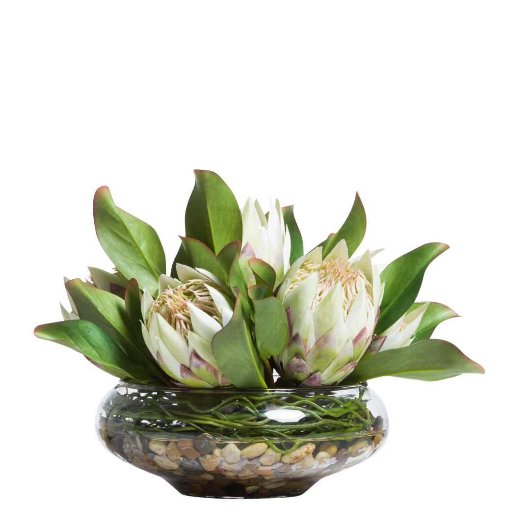 Artificial white protea flowers in a glass bowl with green leaves and decorative stones