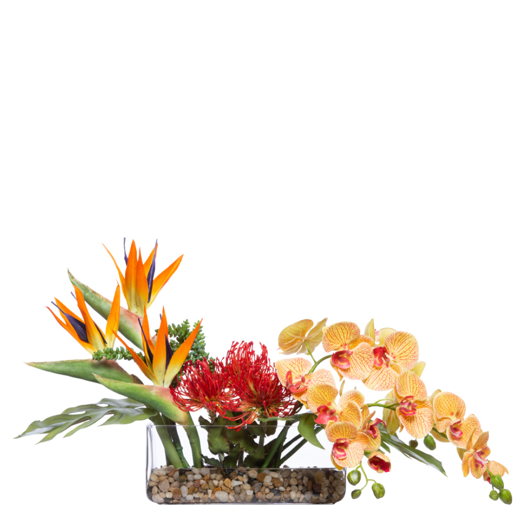 Artificial tropical floral arrangement with orange bird of paradise, red pincushion flowers, and yellow orchids in a clear rectangular vase with pebbles.
