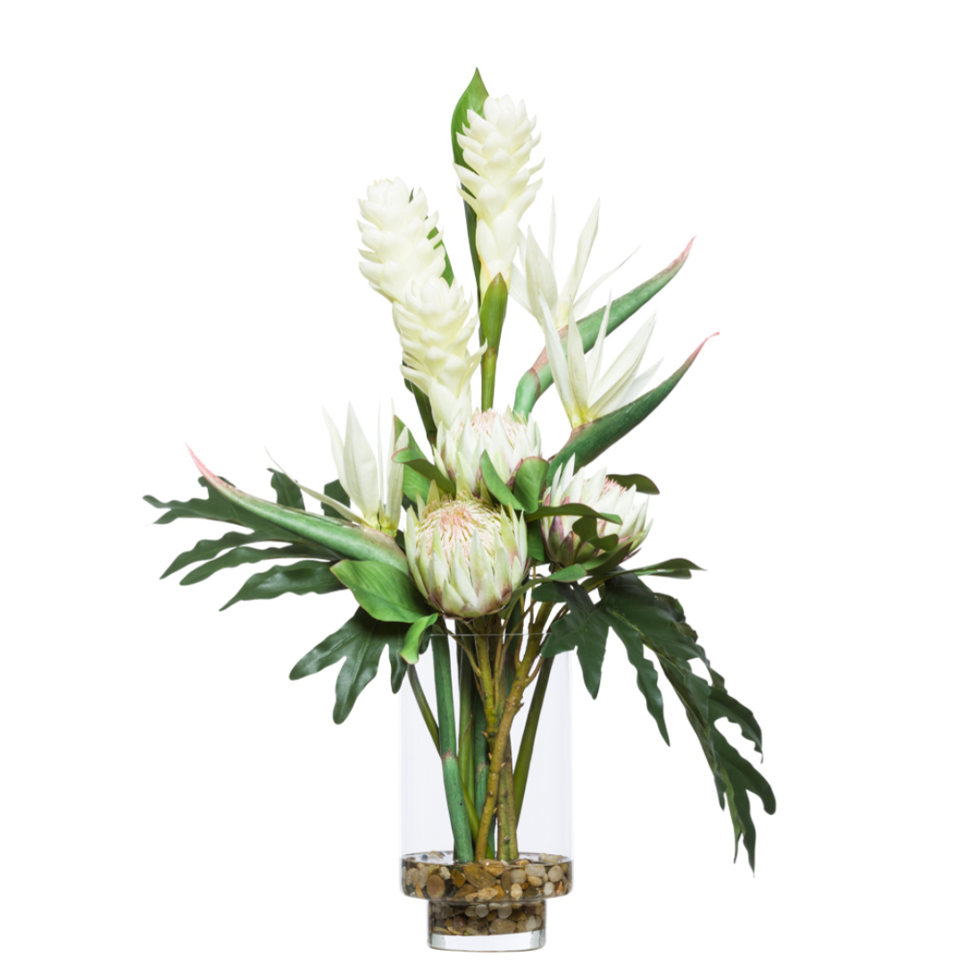 Artificial tropical flower arrangement with white blooms and green leaves in clear glass vase