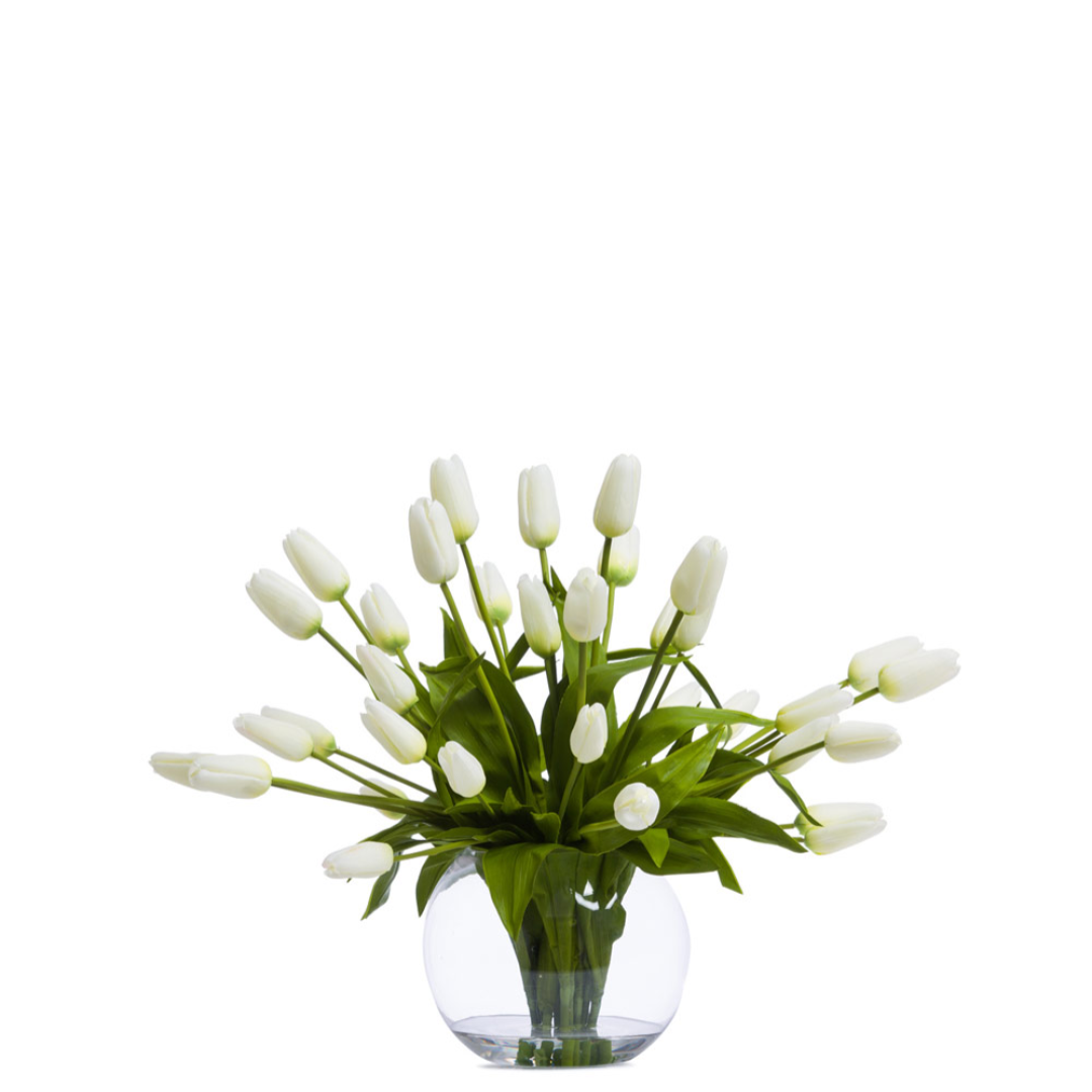 White artificial tulip arrangement in a clear glass vase with green leaves