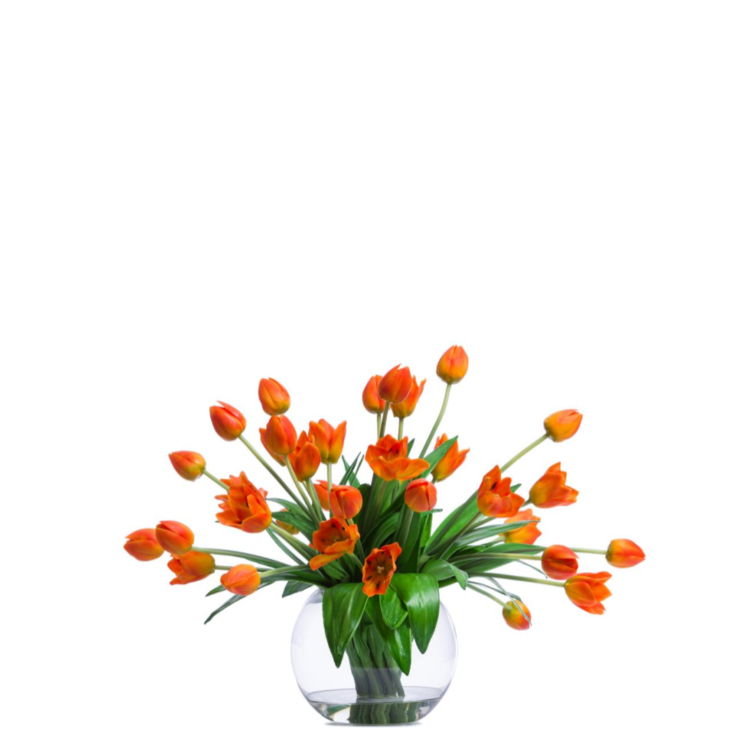 Artificial orange tulip arrangement in a round clear glass vase on white background