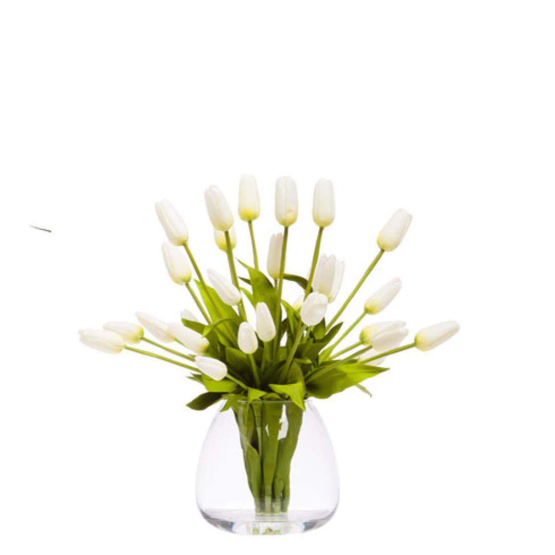 Artificial white tulip bouquet in a clear glass vase with green leaves on white background