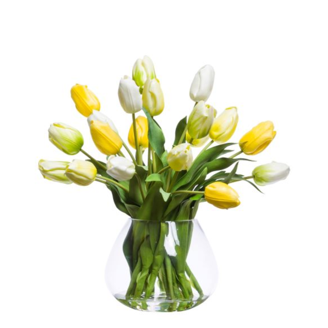 Yellow and white artificial tulips in a clear glass vase on a white background.
