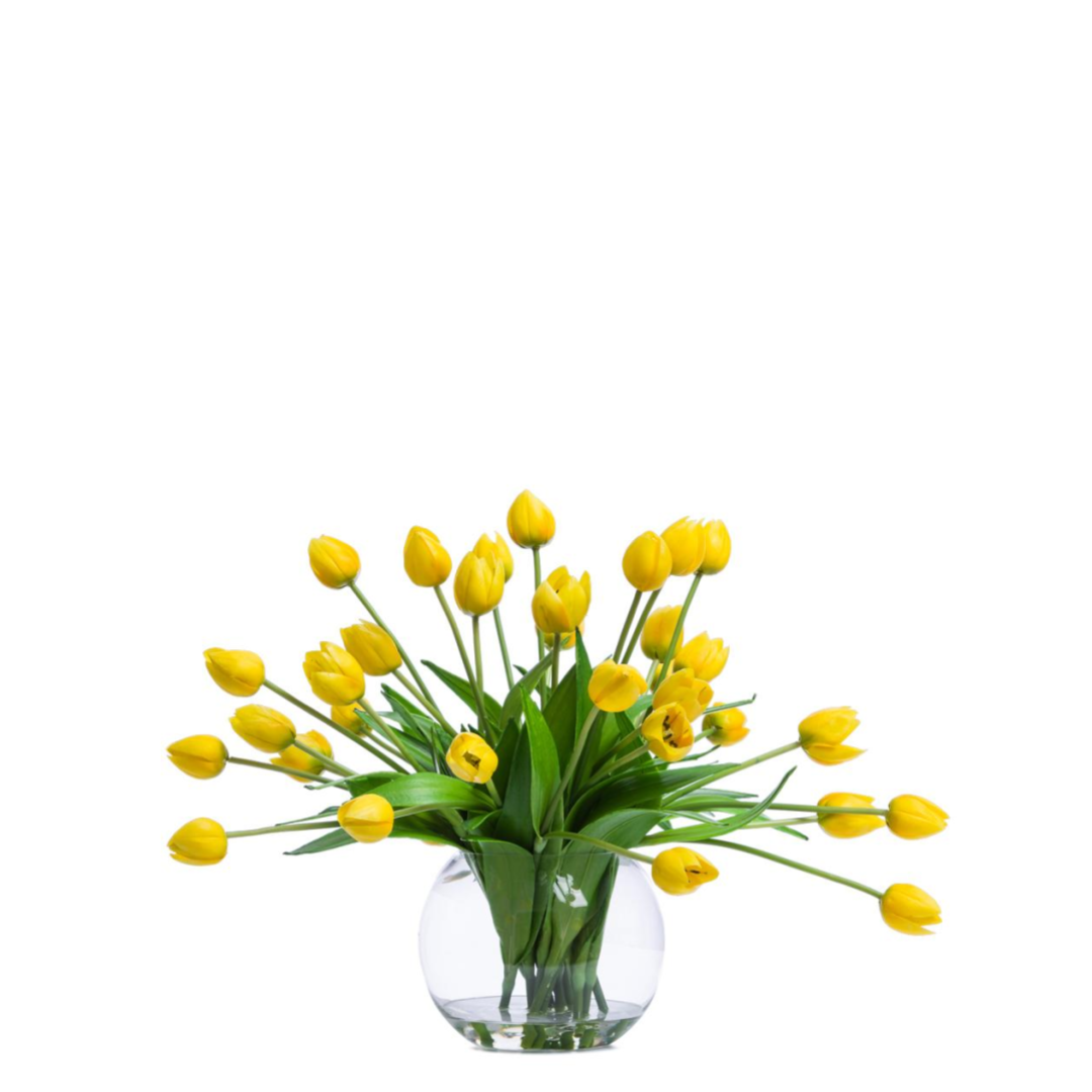 Yellow artificial tulip arrangement in a clear round glass vase, bright and botanical.