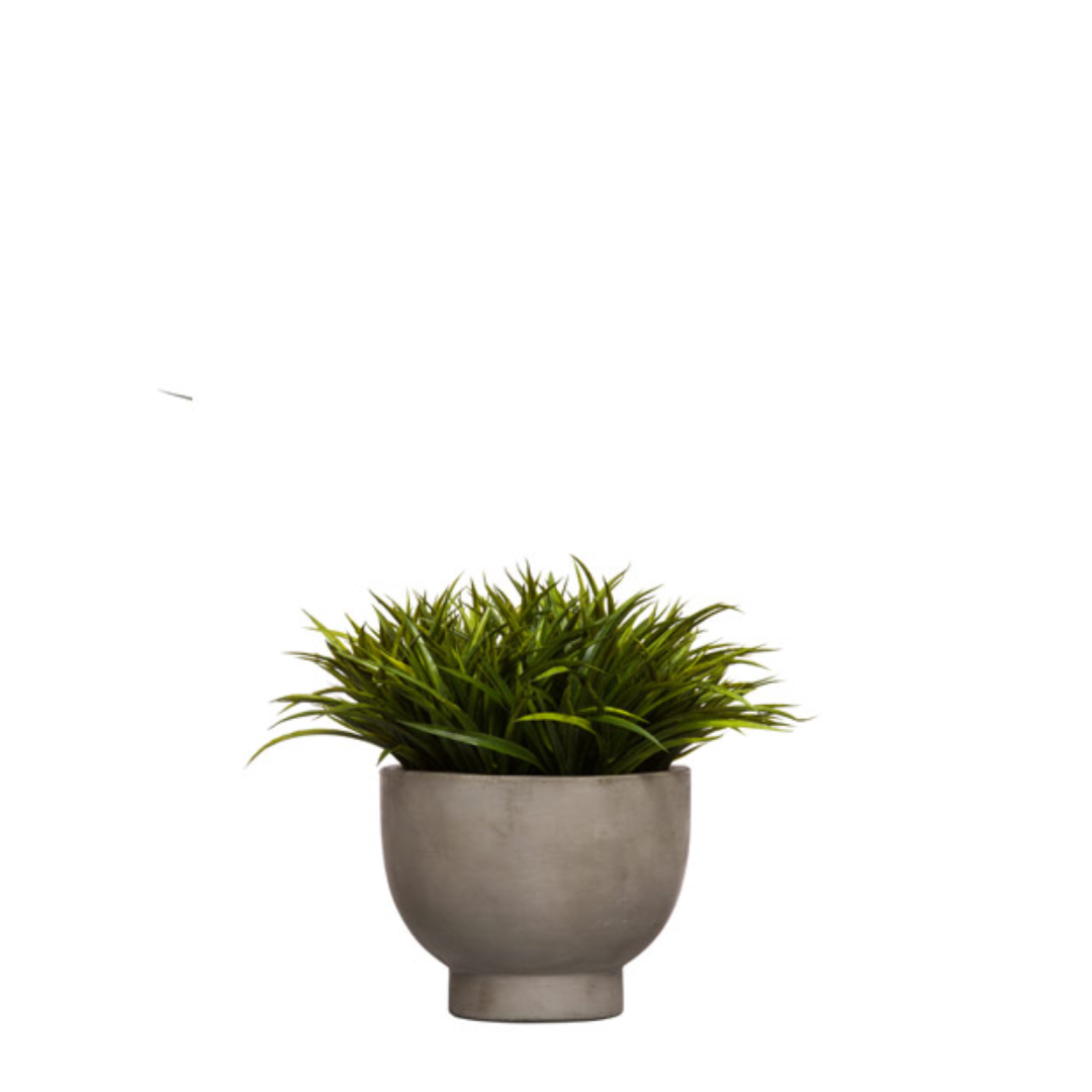 Artificial green grass plant in modern gray round planter on white background
