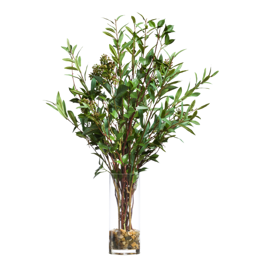 Realistic artificial greenery arrangement with slender leaves in a tall glass vase with stones