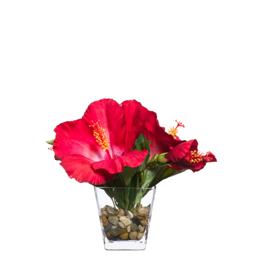 Artificial red hibiscus flower arrangement in a clear vase with decorative stones