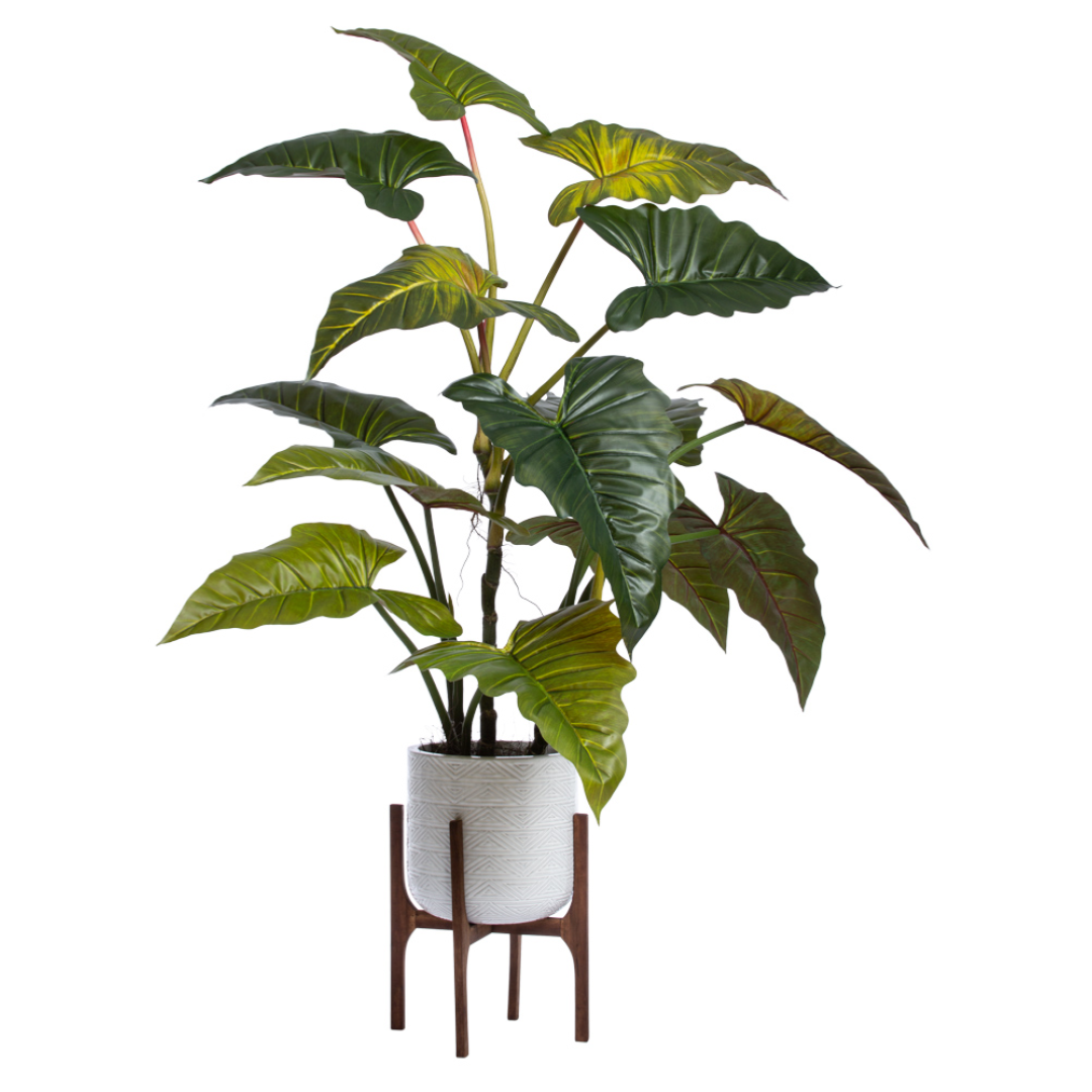 Artificial philodendron plant with large green leaves in a white pot on a wooden stand